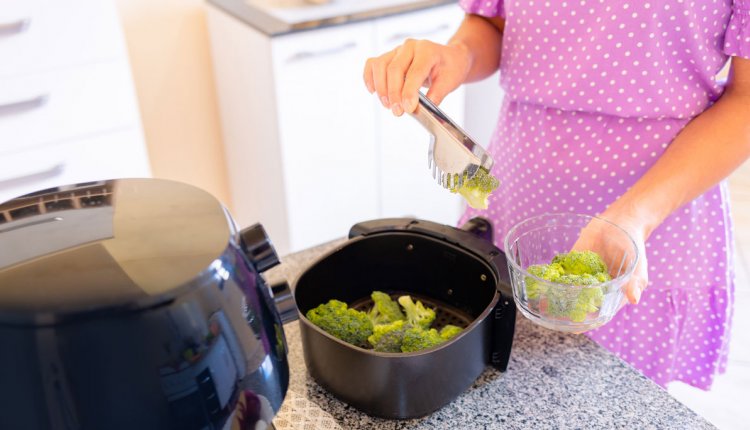 Vrouw in roze jurk doet broccoli in airfryer