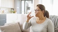 Vrouw zit op bank en neemt medicijn met glas water in