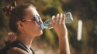 Jonge vrouw met zonnebril drinkt water uit flesje