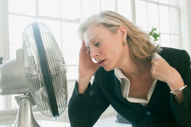 Vrouw heeft het warm en zit voor ventilater om af te koelen